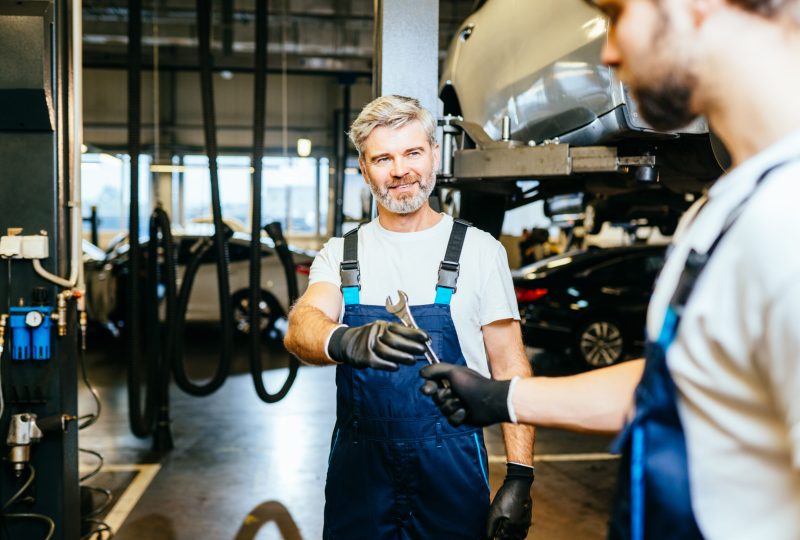 Handing over wrench. Two car mechanics in a workshop repairing car together. Family business concept. Workflow in a car workshop.