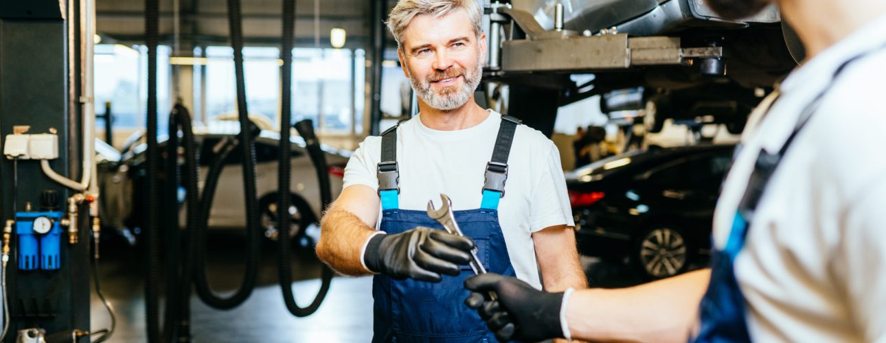 Handing over wrench. Two car mechanics in a workshop repairing car together. Family business concept. Workflow in a car workshop.